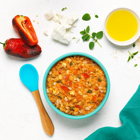 Blue bowl full of Globowl's Medi-Bowl with a spoon and ingredients like olive oil and roasted red peppers surrounding it