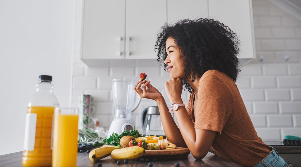 Woman eating strawberry at kitchen counter with healthy foods and juice around