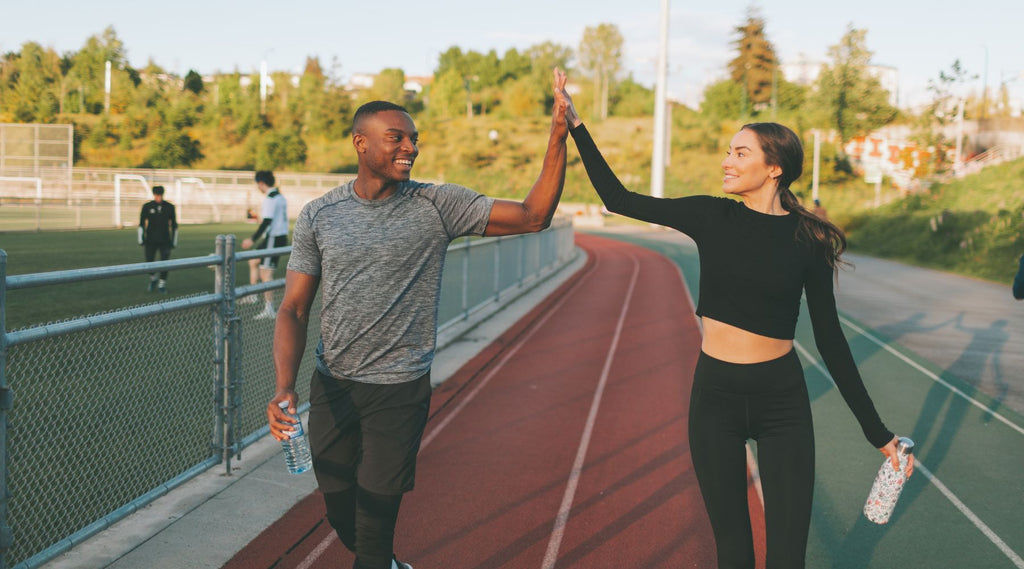 Two people high-fiving on a running track, smiling after a workout