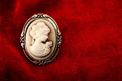 An antique brooch sits on a red velvet stand. 