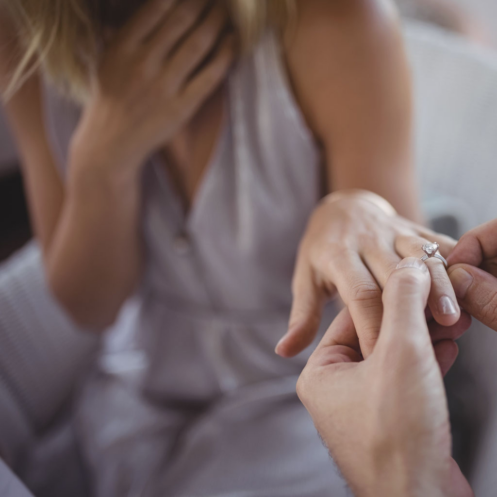 A man puts an engagement ring on a woman's finger during a proposal.