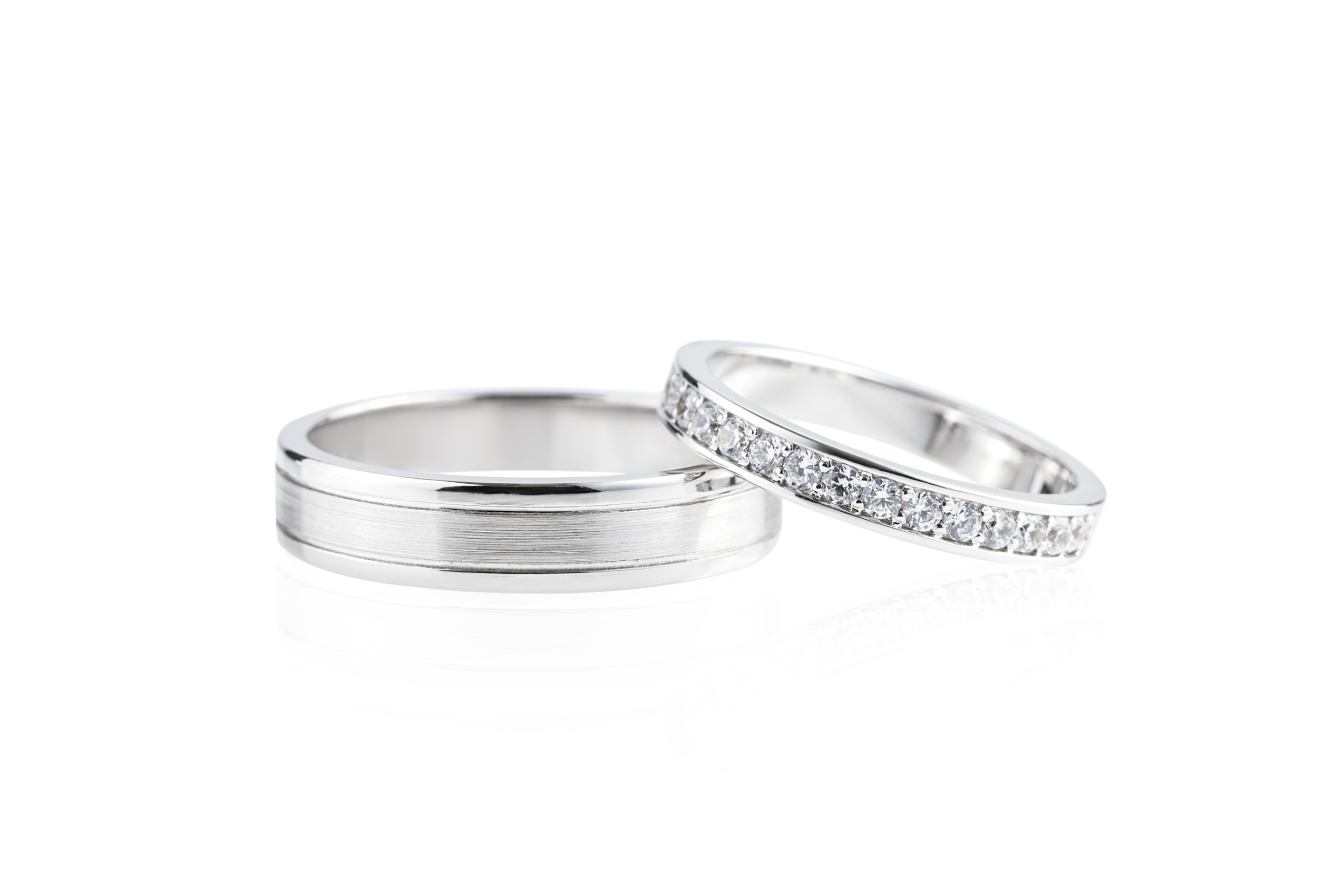 A pair of wedding bands sit next to one another. Both are made of white gold. One of the rings is inlaid with small diamonds. 