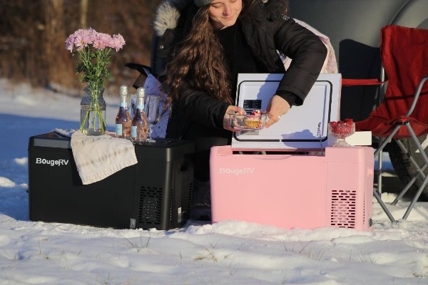 A woman camping in the snow and using BougeRV’s pink and black portable power station-1