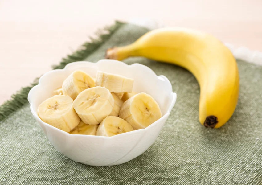 sliced bananas in a white bowl with whole banana on green cloth