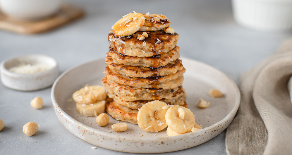 Stapel mit veganen Pancakes mit Banane auf weißem Teller