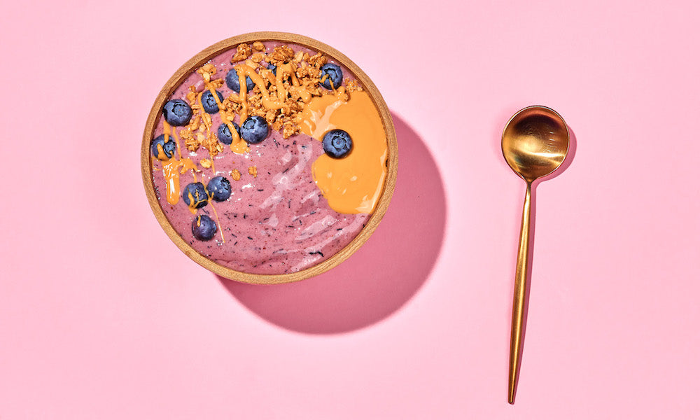 Smoothie Bowl mit Beeren und Löffel auf rosa Hintergrund