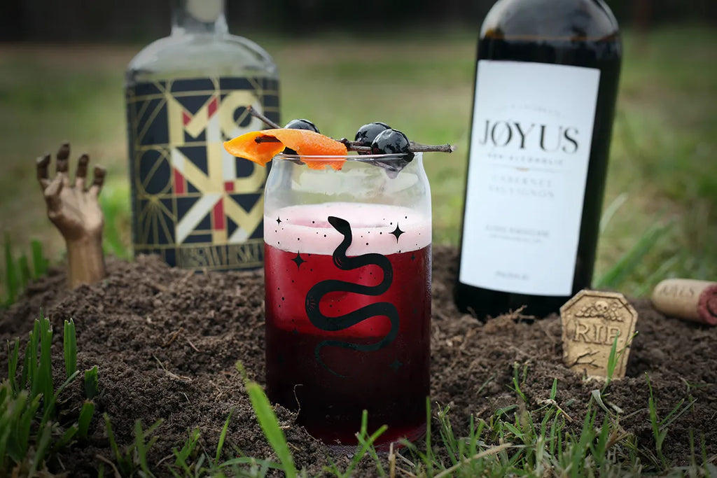 Joyus non-alcoholic cabernet sauvignon in a dark and spooky photo with the Red Moon Over Manhattan non-alcoholic cocktail in a snack embossed glass in the foreground
