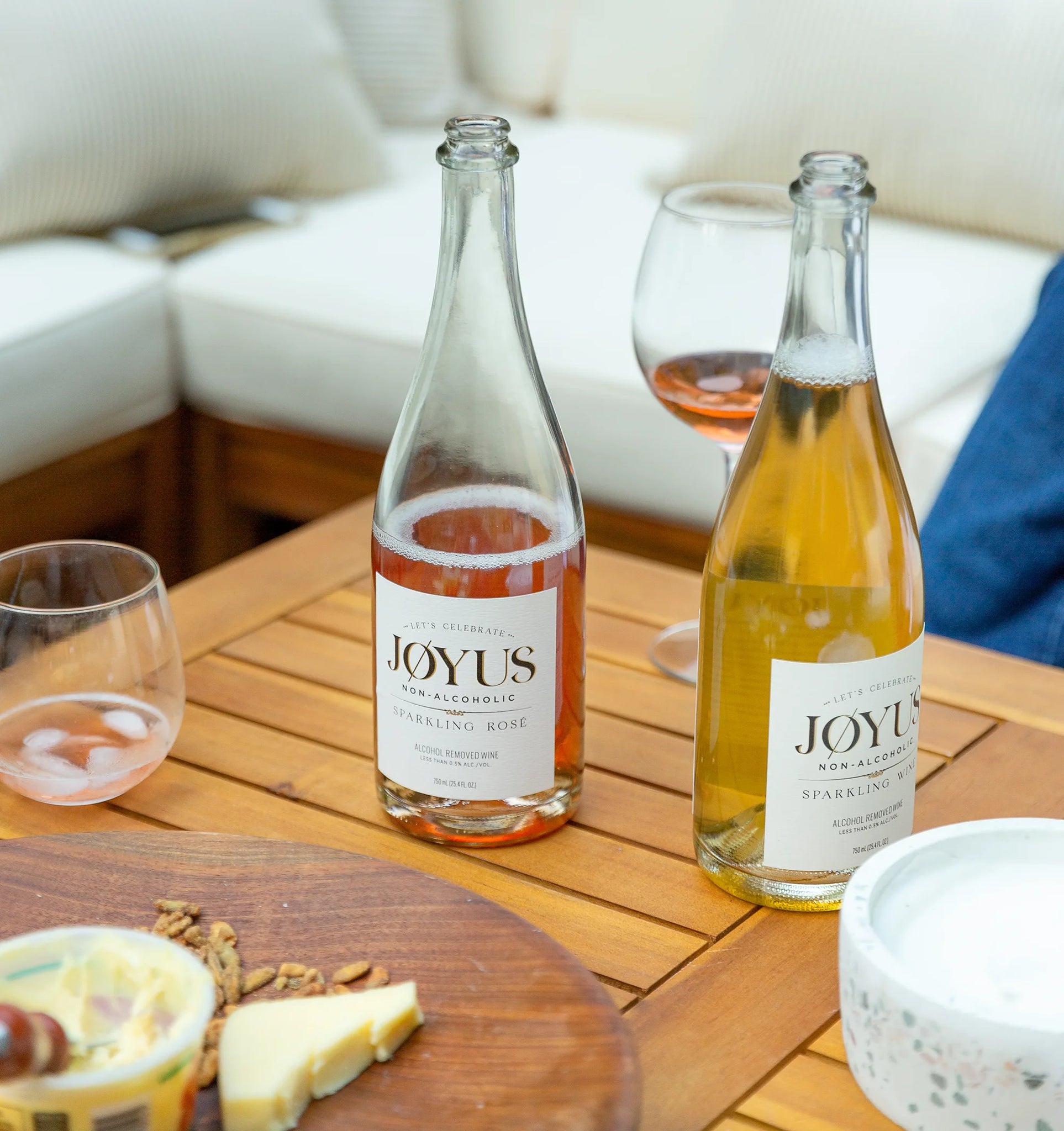 Bottles of Joyus non-alcoholic sparkling wine and sparkling rose sitting on a table with cheese