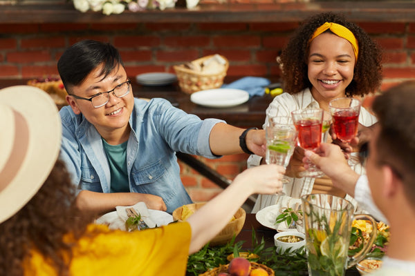 Four friends sit around a table and cheer with non-alcoholic mocktails