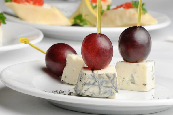 three separate roquefort cheese blue cheese appetizers cubed and skewered with grapes on top.