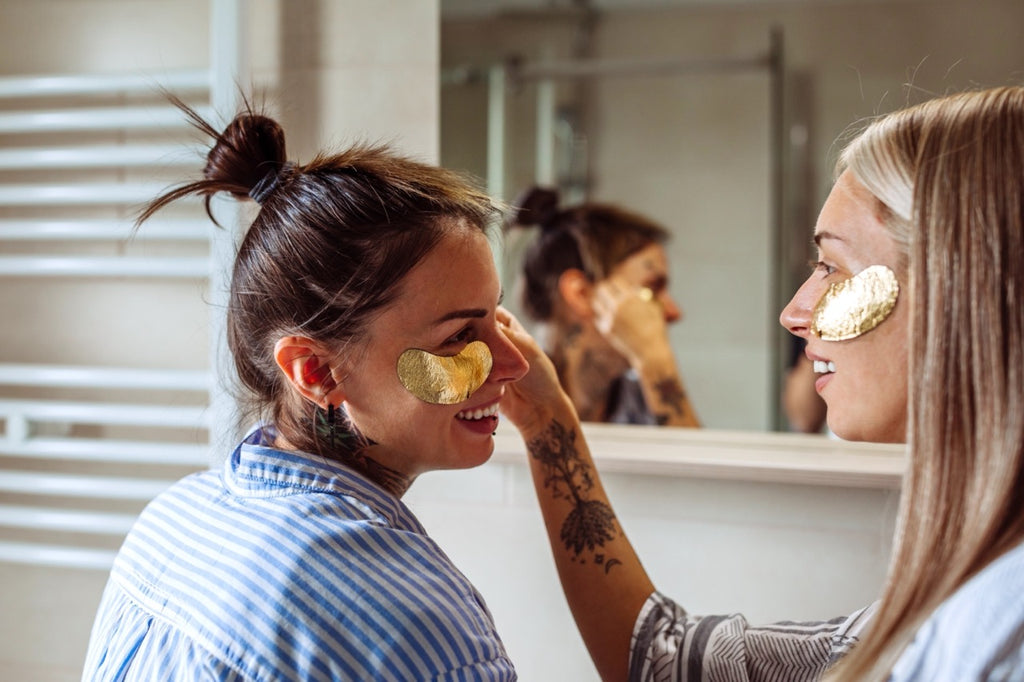 Two women putting golden eye masks on each other