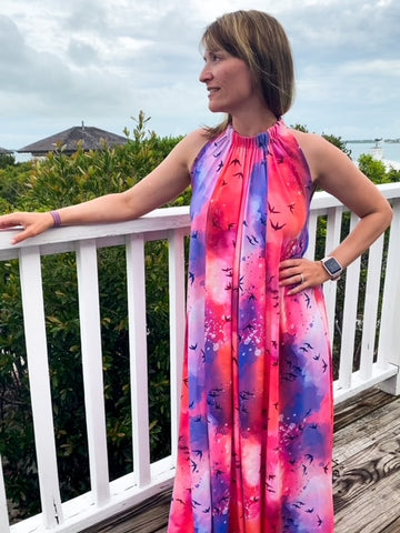 A girl wearing a pink and blue modeled dress with dark maroon birds on it.