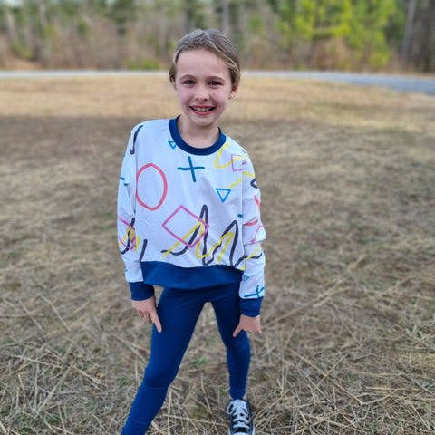 A girl wearing a sweater with doodled lines, squares, circles, and x's in various colors.