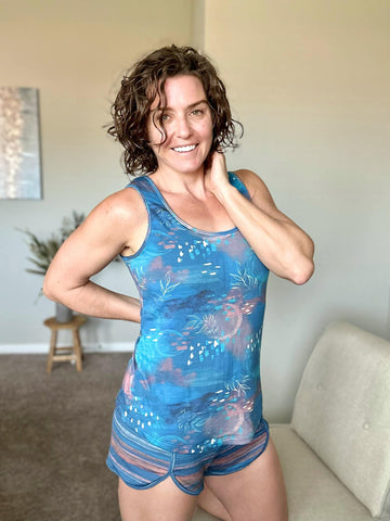 A girl wearing a blue top with peach watercolor circles and white leaves. She is also wearing blue and orange stripped shorts