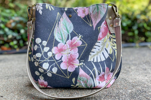 A handbag with a black background and pink flowers with green and peach leaves inside a gold cage