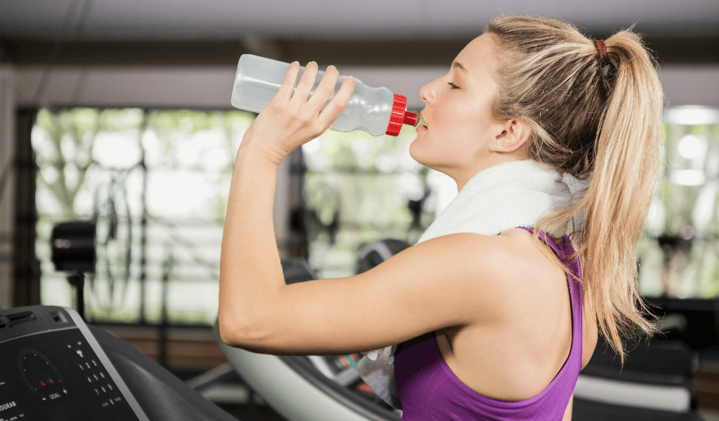 a girl drinks from a water bottle at the gym