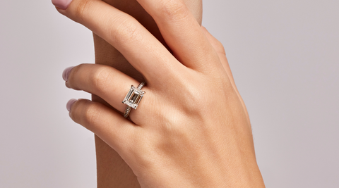 Emerald engagement ring on hands with plain background.