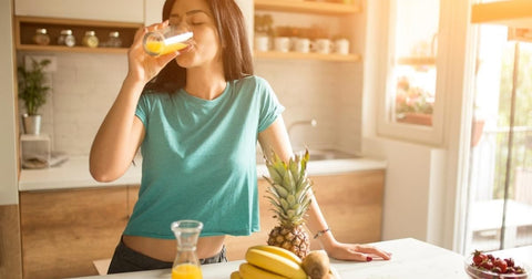 woman drinking a glass of orange juice in her kitchen in the morning - splashpad self care