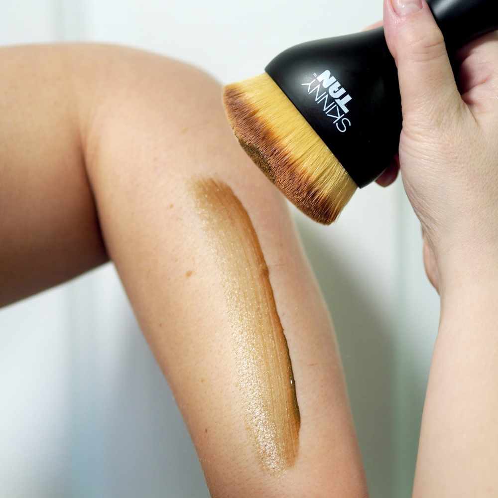 A person applying Skinny Tan's 1 Day Instant Tanner with the new Body Buffing Brush