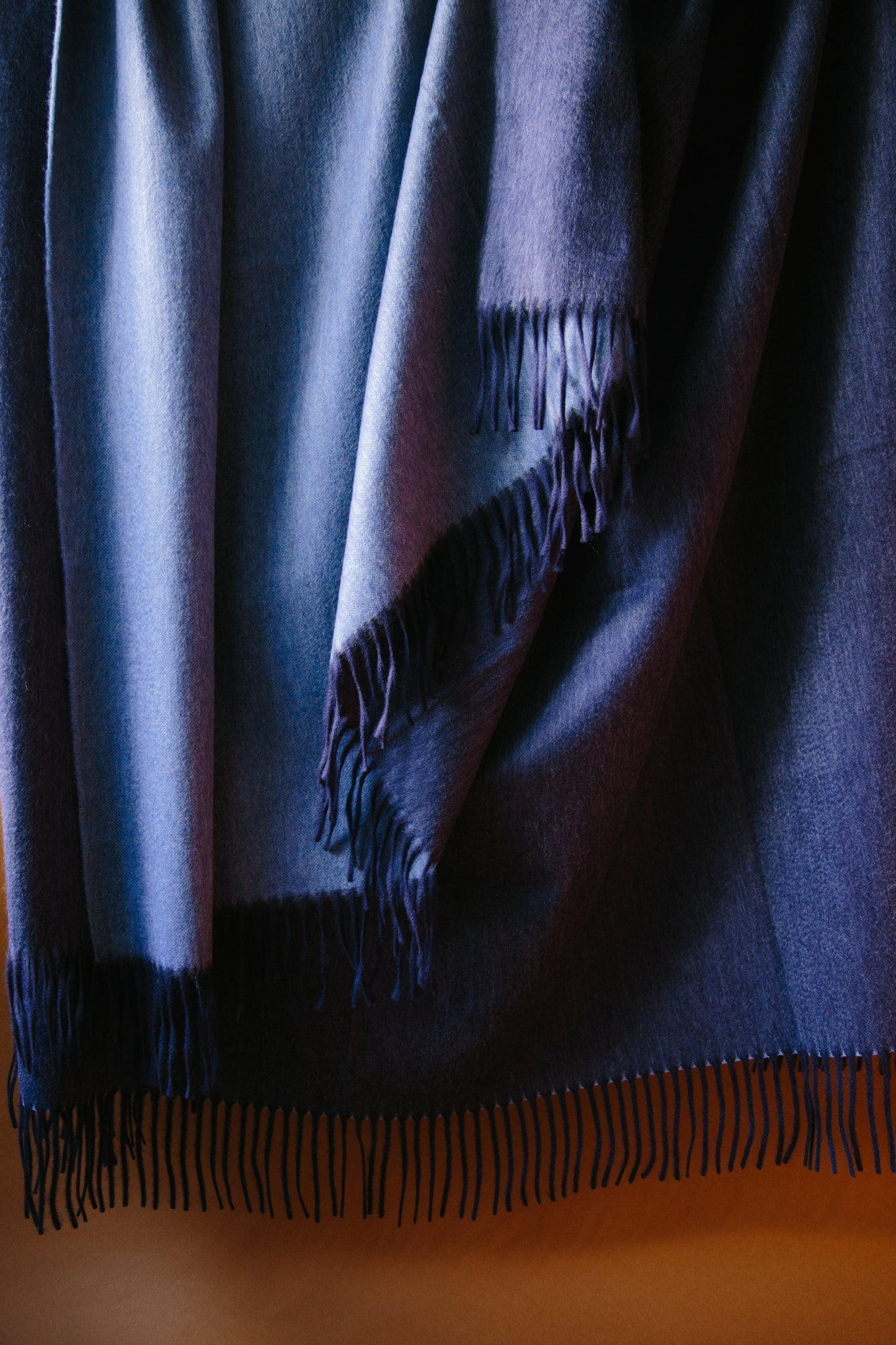 Large cashmere throw. Two sided reversible colour; navy and denim blue. Draped against a brown background with natural light.