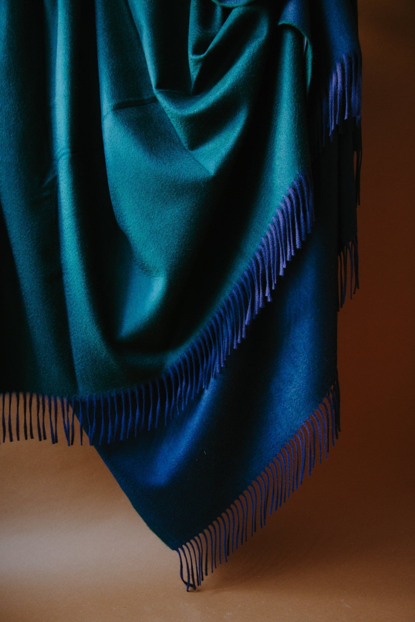 Large cashmere throw. Two sided reversible colour; forrest green and navy. Draped against a brown background with natural light.