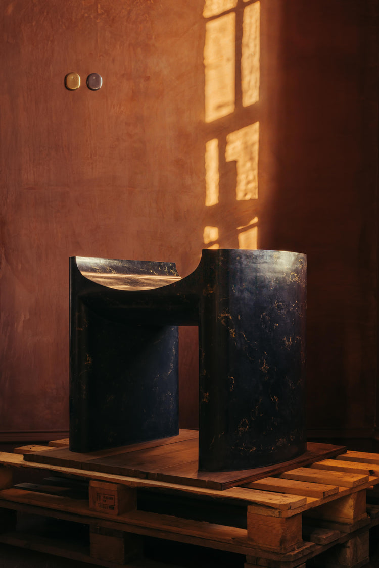  A large plaster black chair, named Cat Throne, and made by Chalk Plaster. The Throne is sat on top of a pallet as part of The Grit and The Glamour exhibition at Bard..