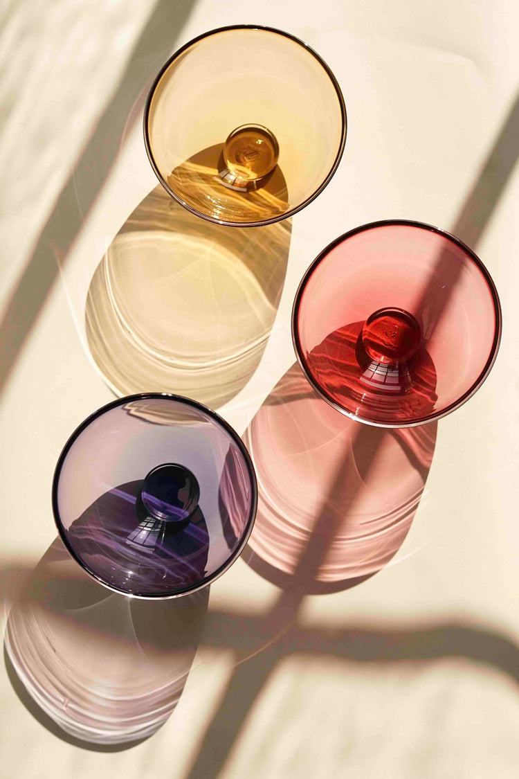 Three Lindean Mill glass Gem Bowls in amber, blush pink and violet. The shot is taken looking down on the bowls. You can see the glass foot the bowl sits on and the rings within the handblown nature of the glass.
