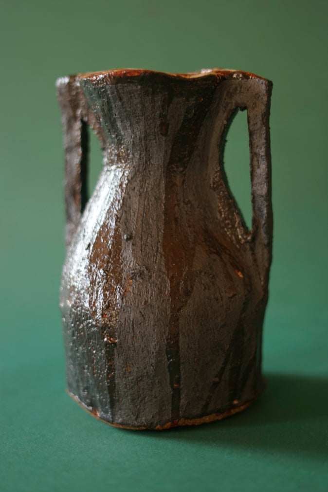 A vase from Morven Muglrew's series, 'Running out of steam'. Black and ochre in colour, rich in texture. Photographed against a green background at Bard Scotland in Leith, Edinburgh.