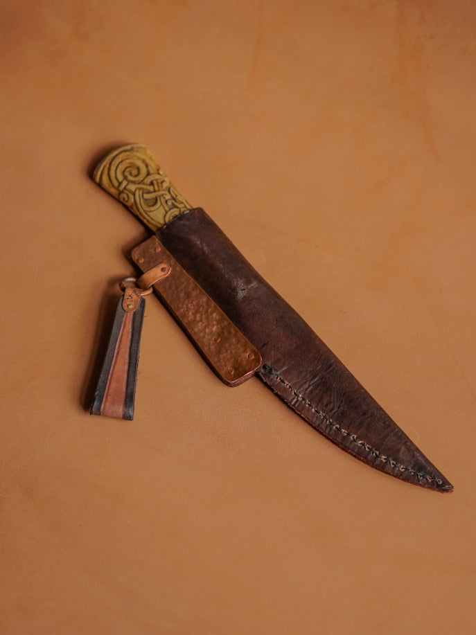 The blade is sheathed in a hand-stitched and tooled scabbard of light cowhide, reinforced with hammered copper placquets and copper suspension rings.