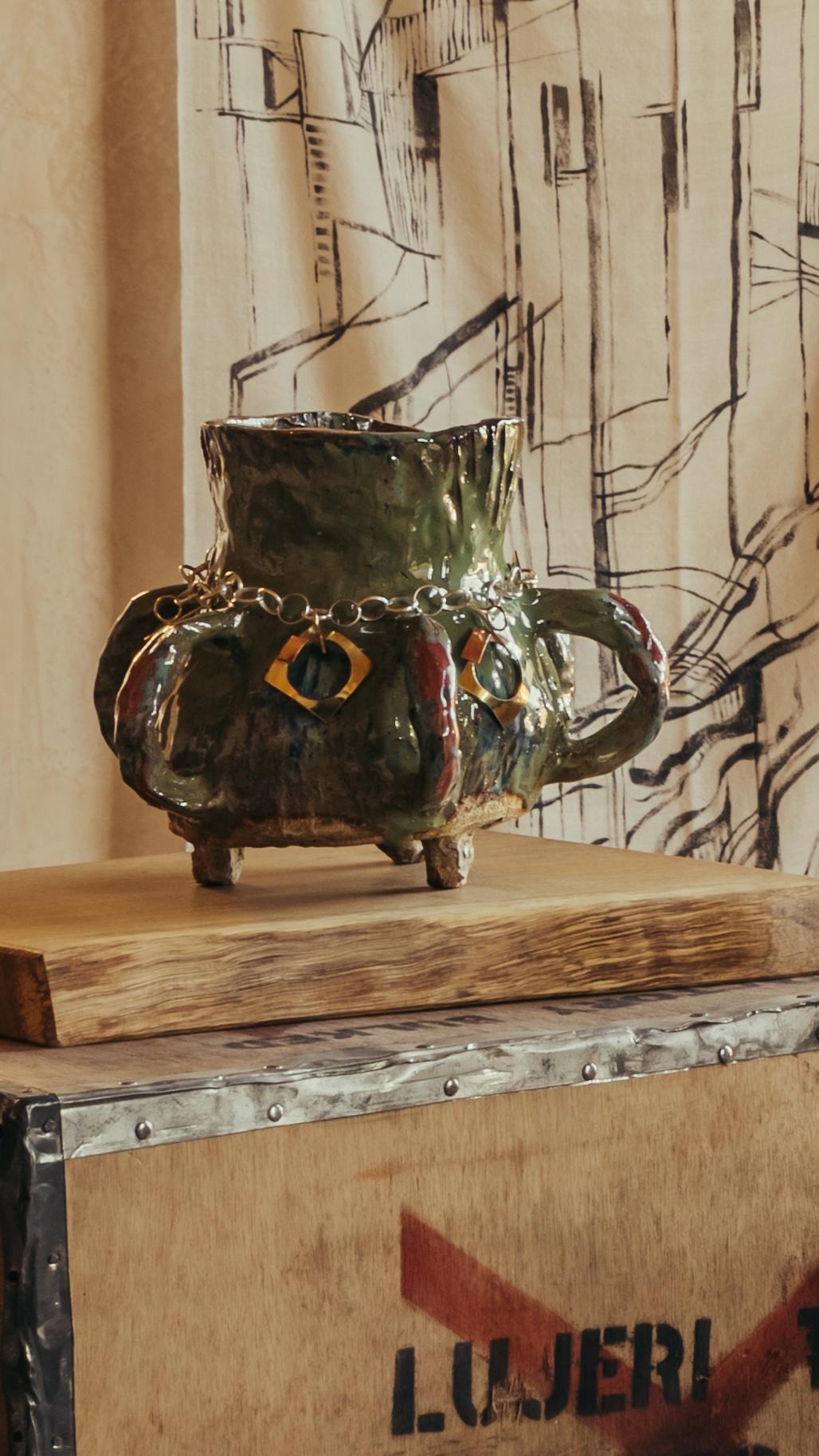  Ceramic vase with handles and feet by Glasgow based ceramicist and artist Morven Mulgrew. The vase sits on top of a wooden plank, and vintage tea box, as part of The Grit and The Glamour exhibition at Bard Scotland.