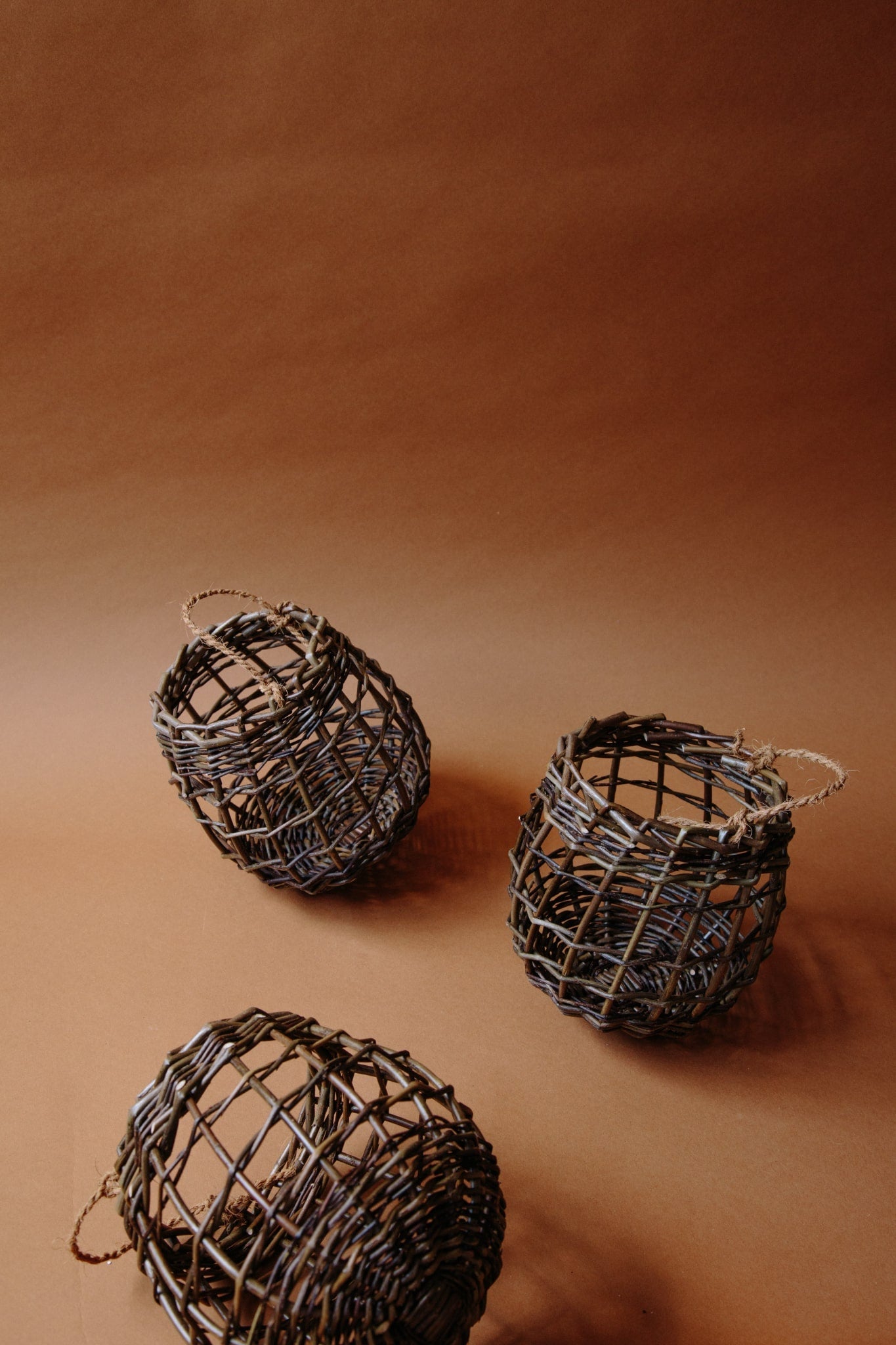 Small fruit and vegetable pots woven from willow with string handles. Three shown in frame, on a brown paper background. 