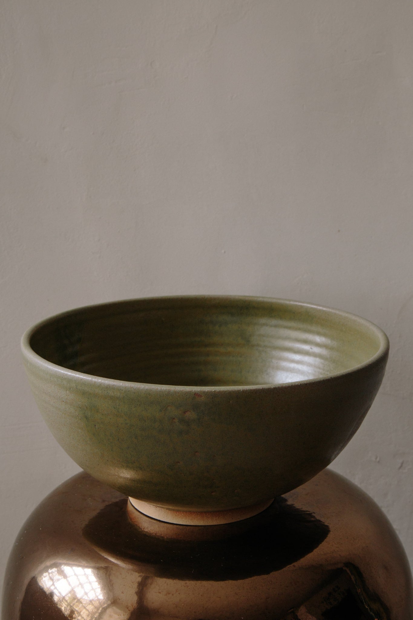 Large olive green ceramic bowl placed on a metallic copper stool photographed in natural light coming in from the left.