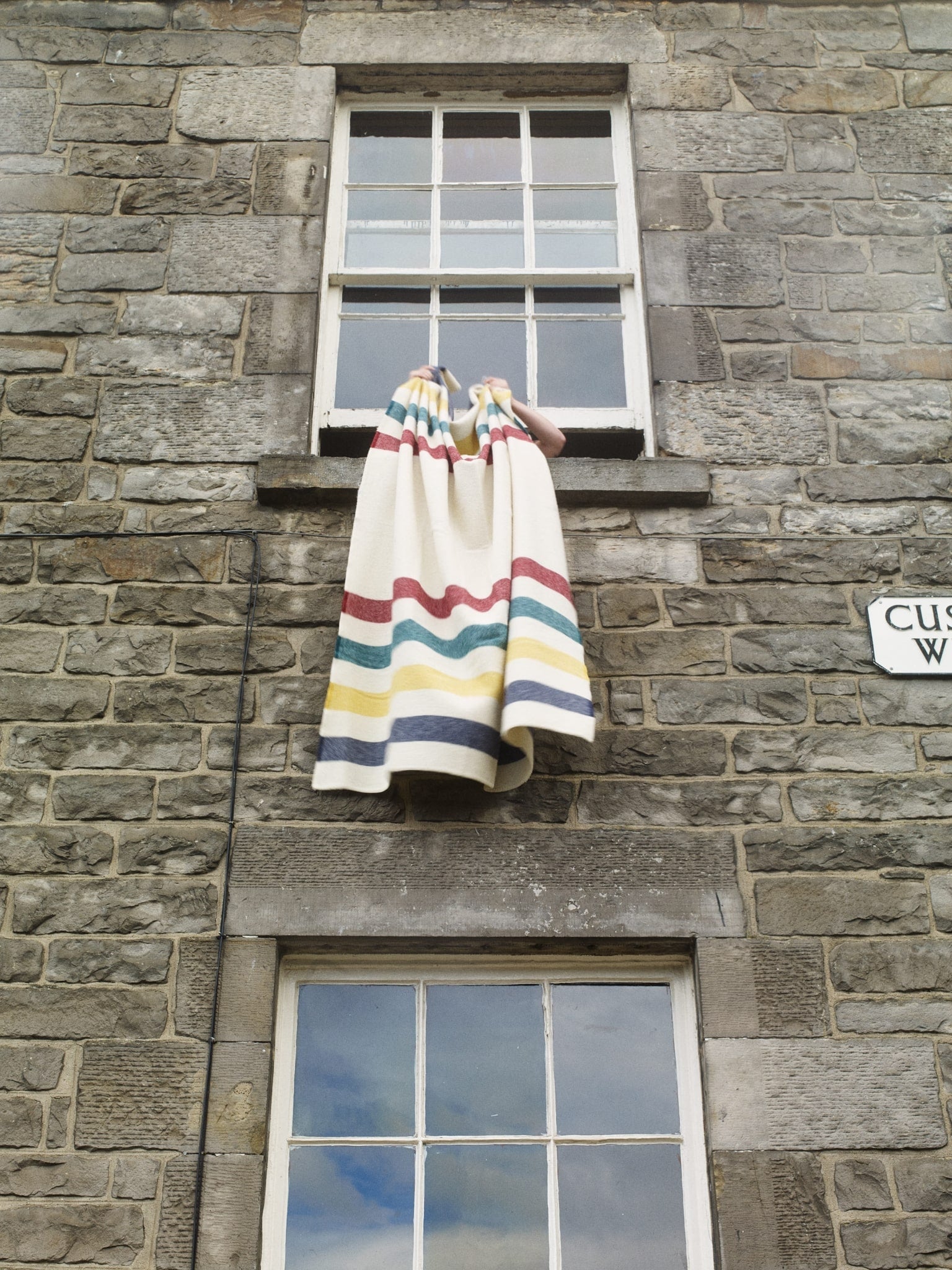 A multi coloured striped lambswool blanket is held out of the window of an old brick building. Customs Wharf, in Leith, Edinburgh.