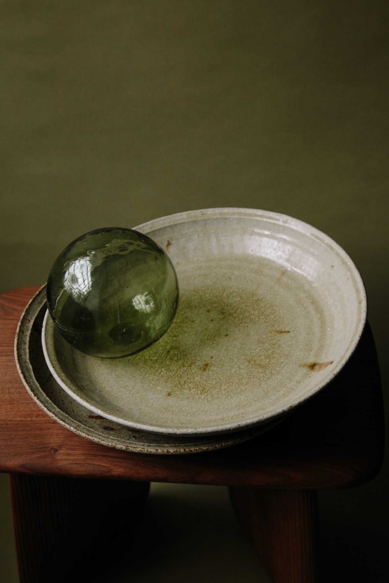 A stack of unique green ceramic platters with a green glass sphere balanced on the top platter. The glaze being reflected in natural light.