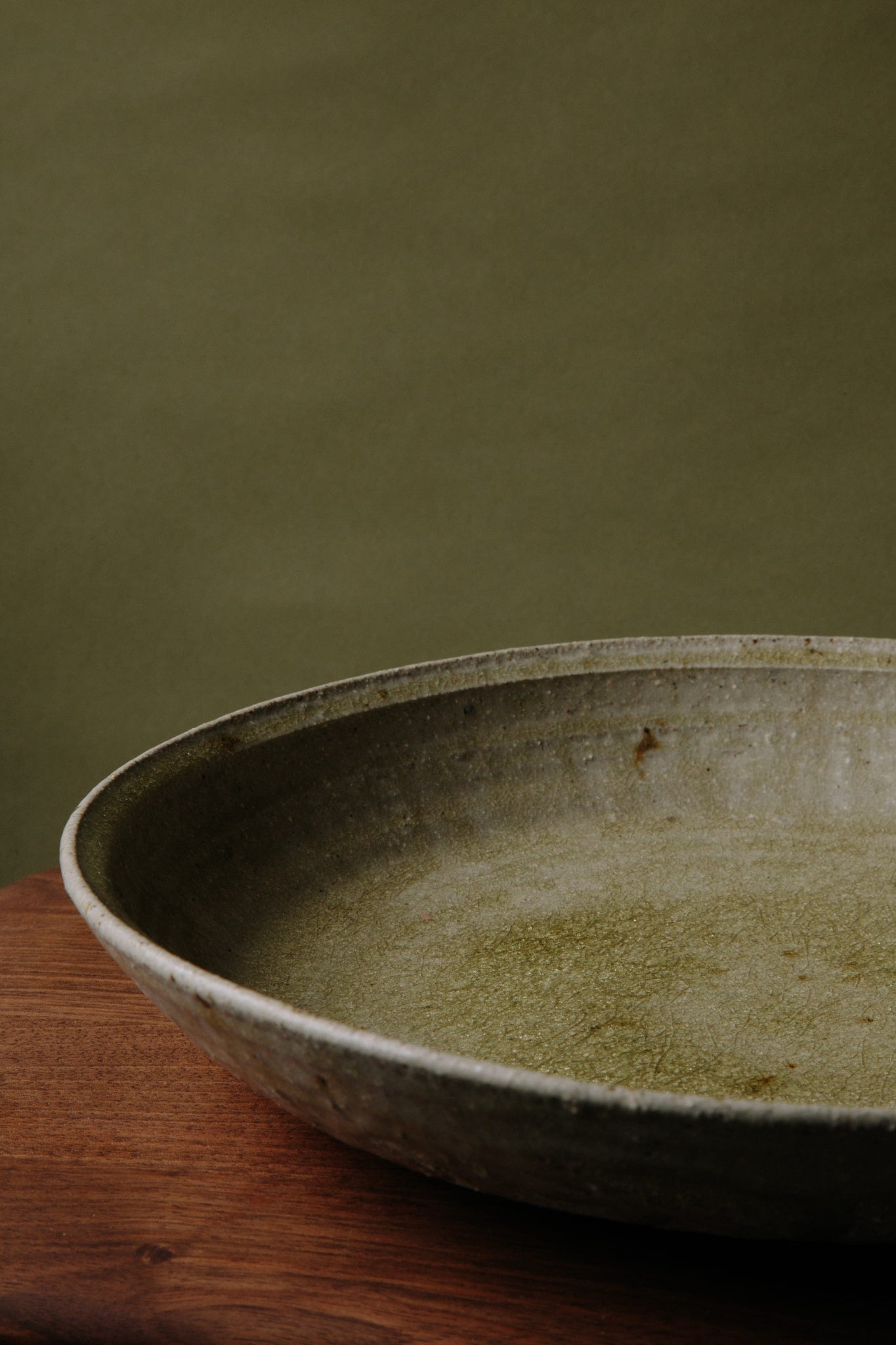 A side view of an ash glazed ceramic platter by Jonathan Wade. The depth of the platter can be seen as well as the mottled surface.