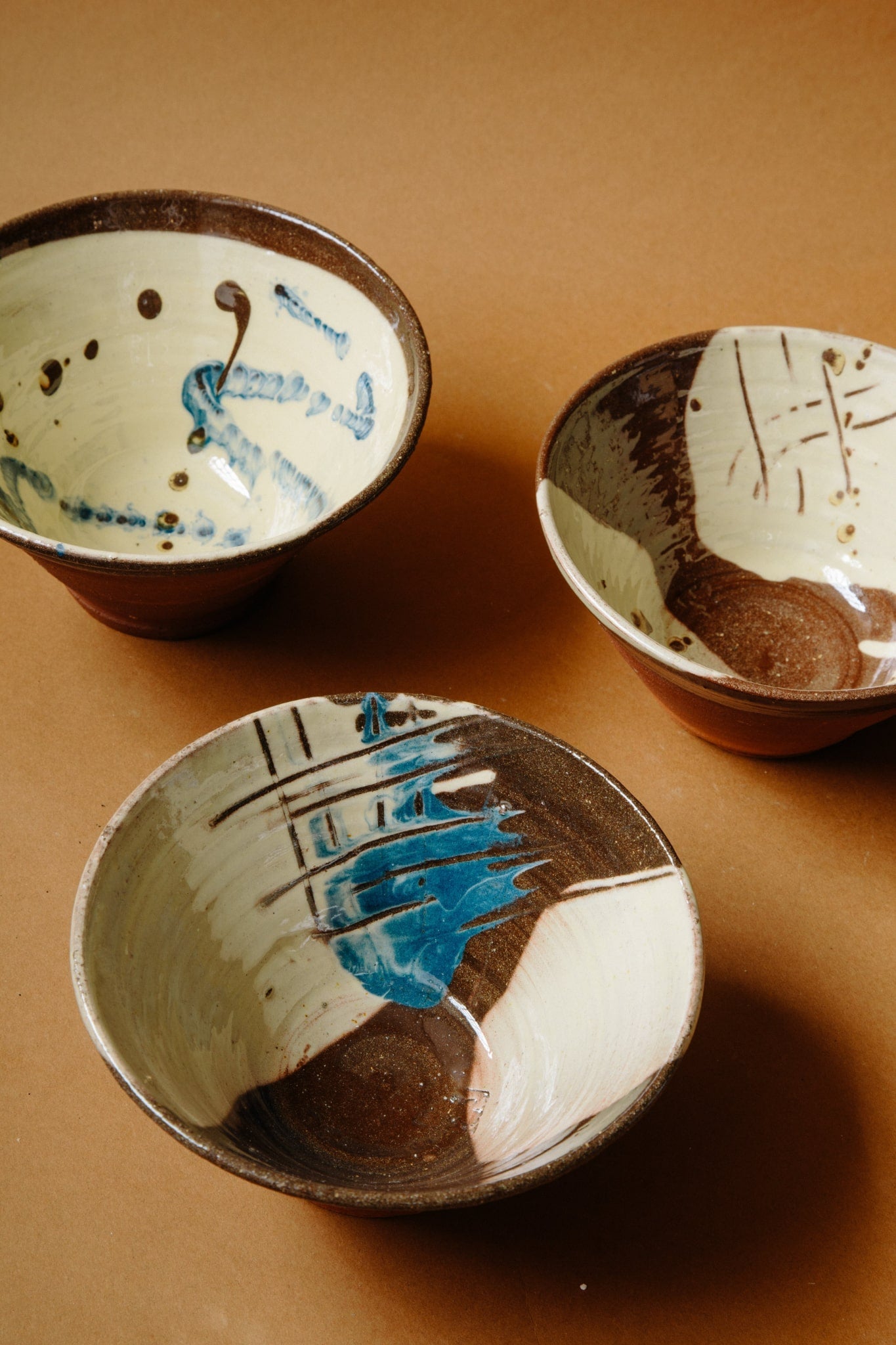 Three unique terracotta bowls. Mainly white and brown in colour, but with additions of deep blue and expressive painterly marks and scratches. 