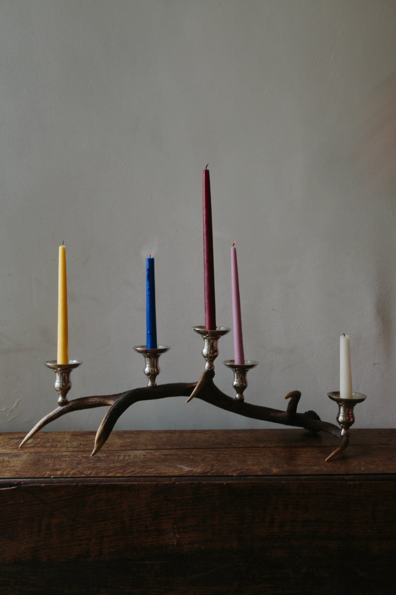 Antler candelabra with five chrome candlestick cups with candles just recently blown out so smoke is visible.
