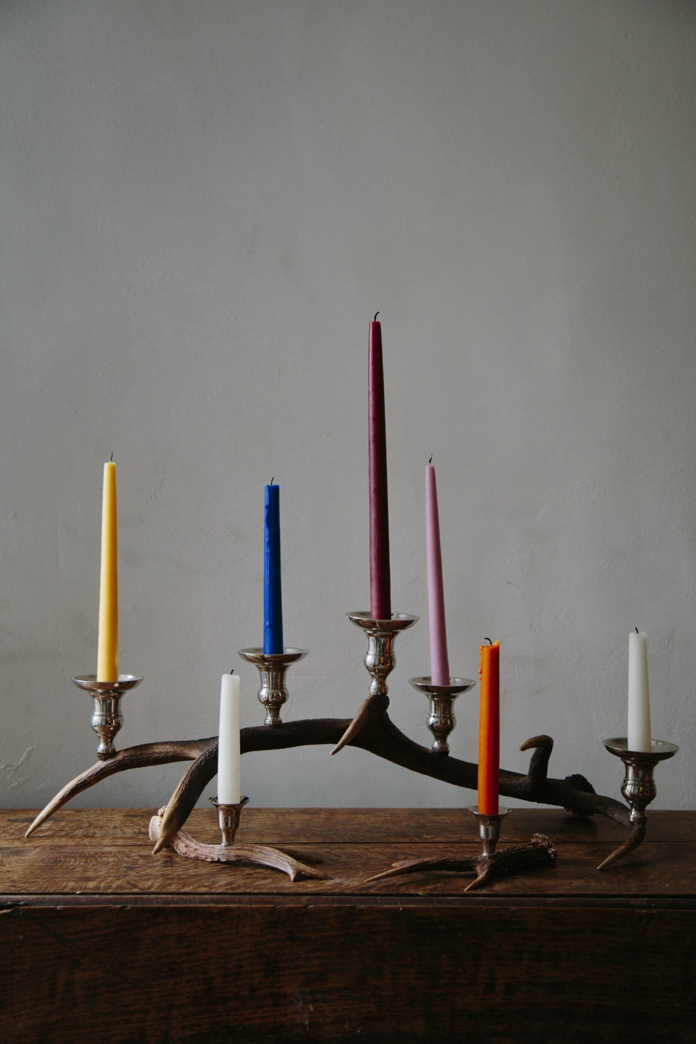 A display of candlesticks and candelabras on a wooden table top. Styled with colourful candles.