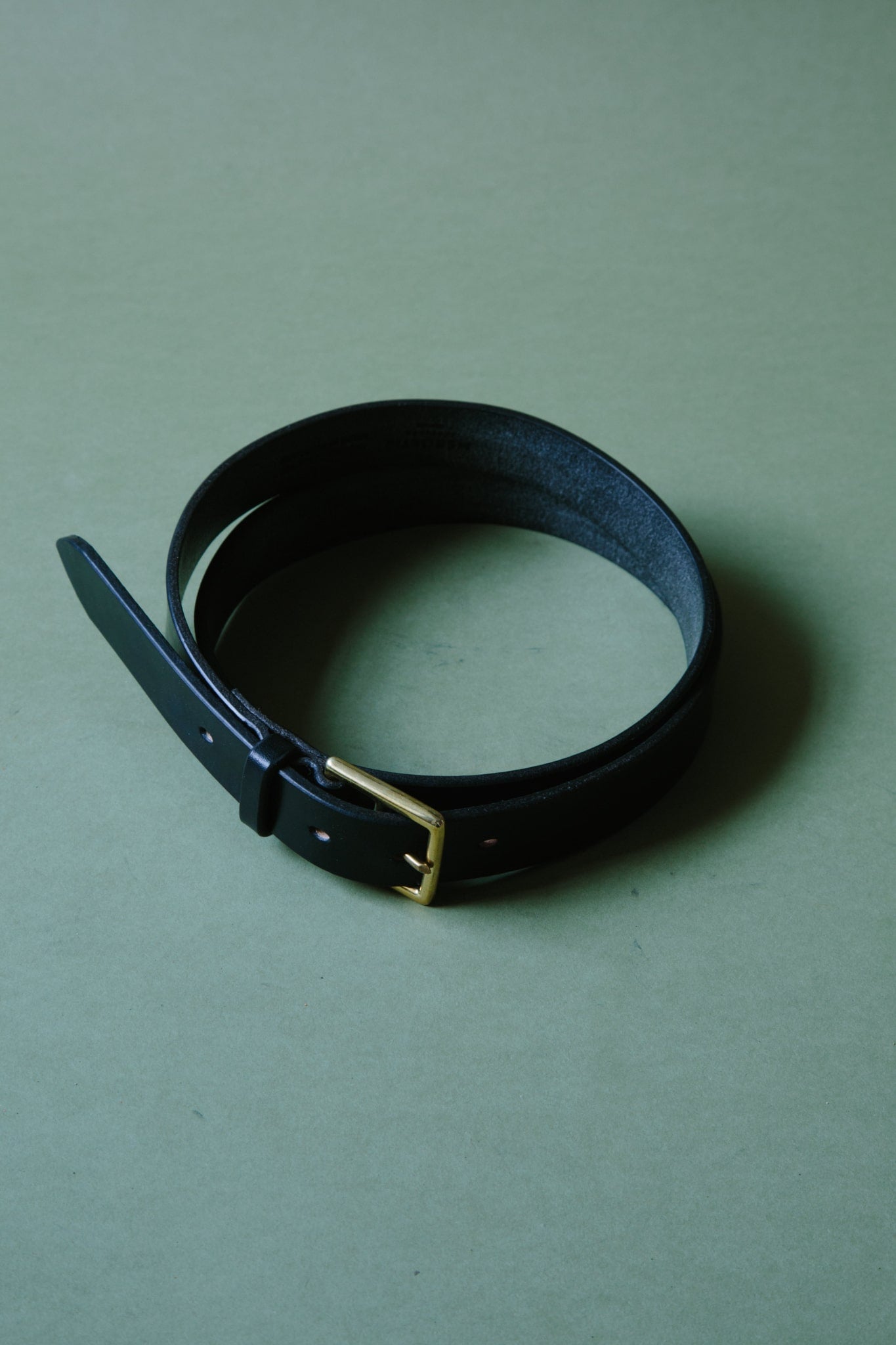 A black bridle leather belt, wrapped into a circle so it fits within frame. The metal belt is buckle can be seen.