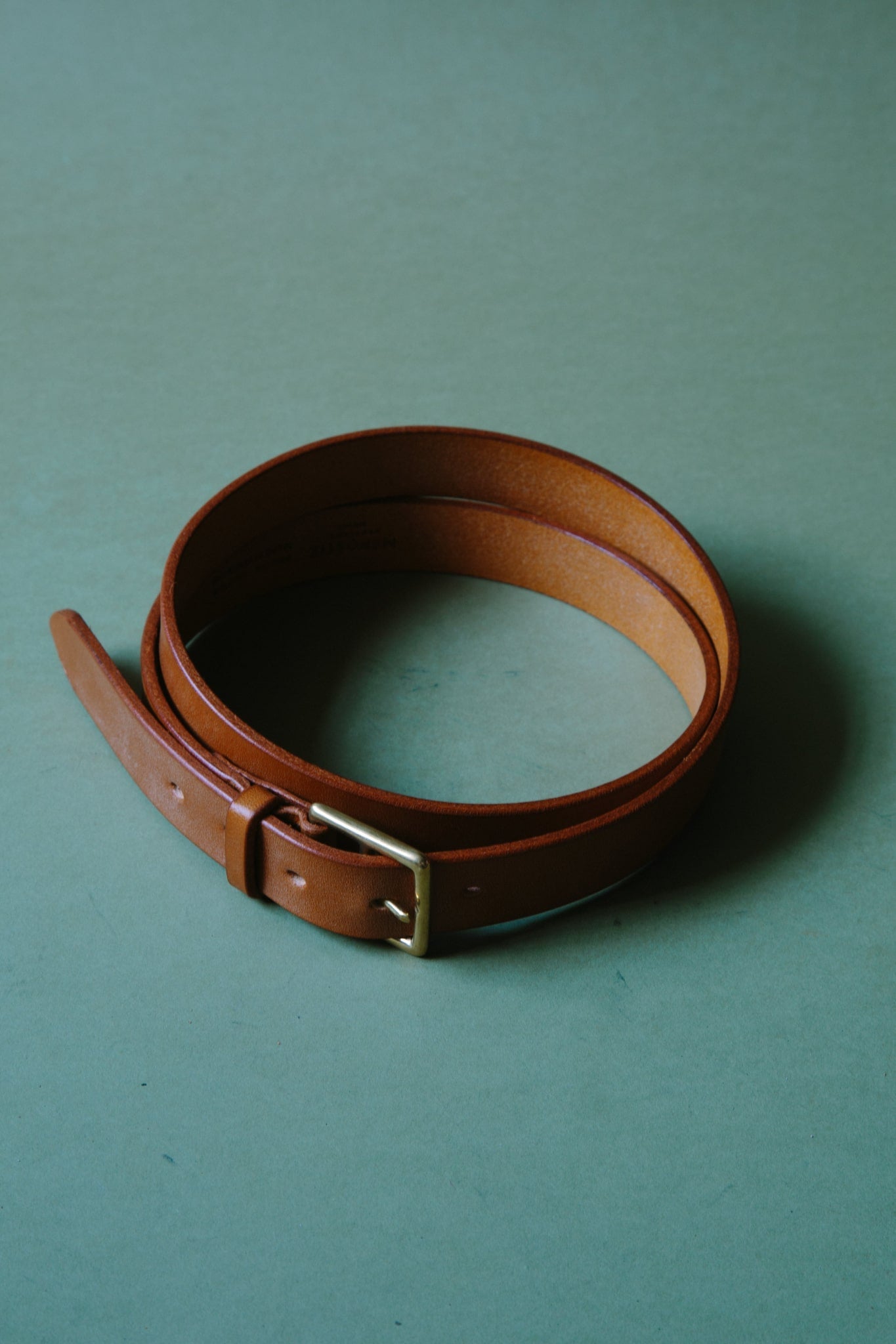 A tan bridle leather belt, wrapped into a circle so it fits within frame. The metal belt is buckle can be seen.