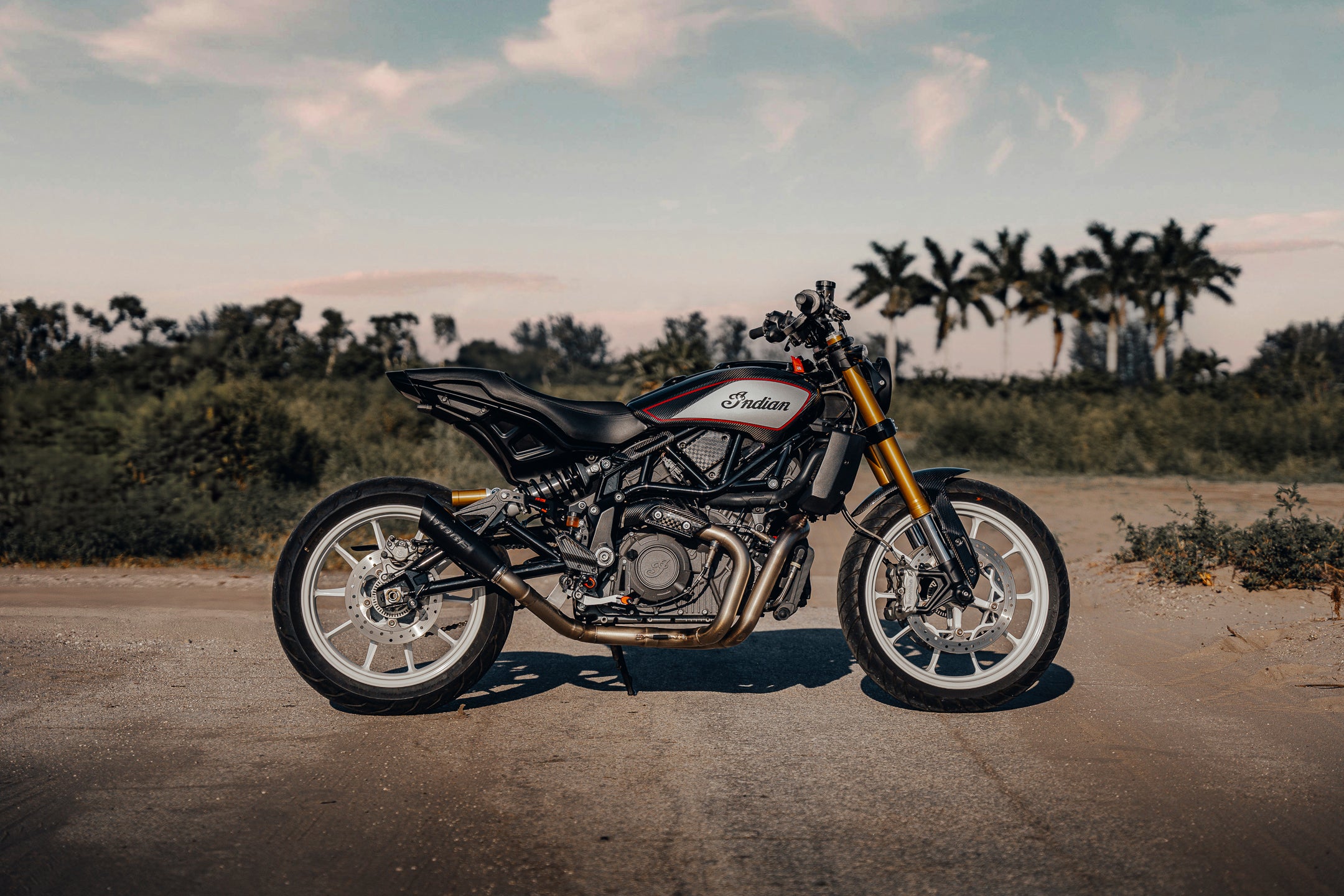 A black Indian motorcycle parked on a road with palm trees in the background.