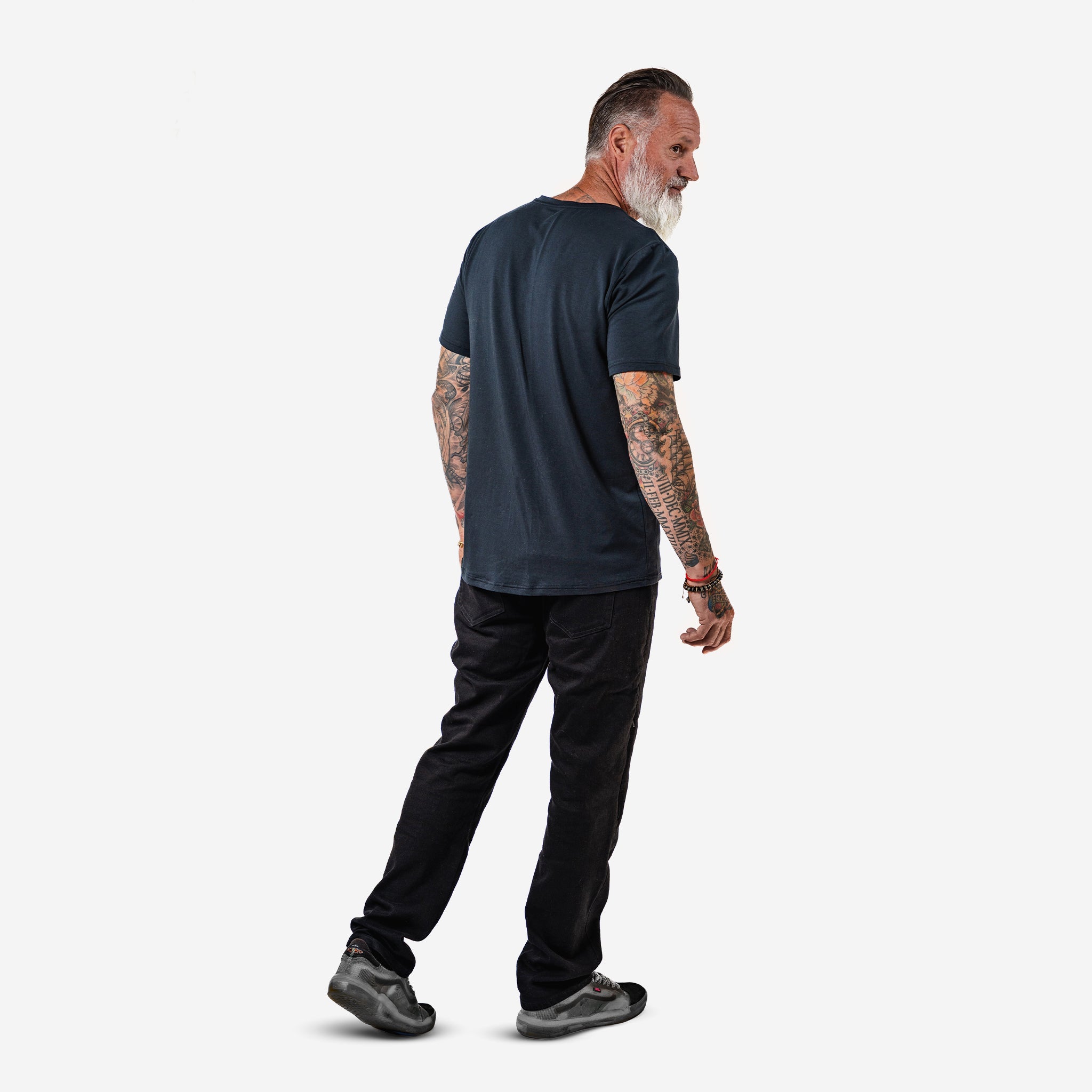 Bearded man with tattoos walking against a white background.