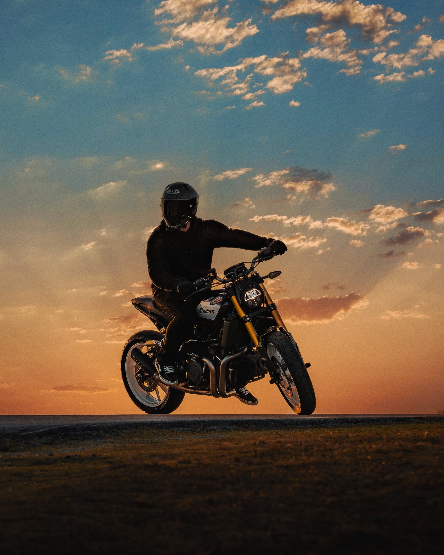 Motorcyclist riding at sunset with a cloudy sky in the background.