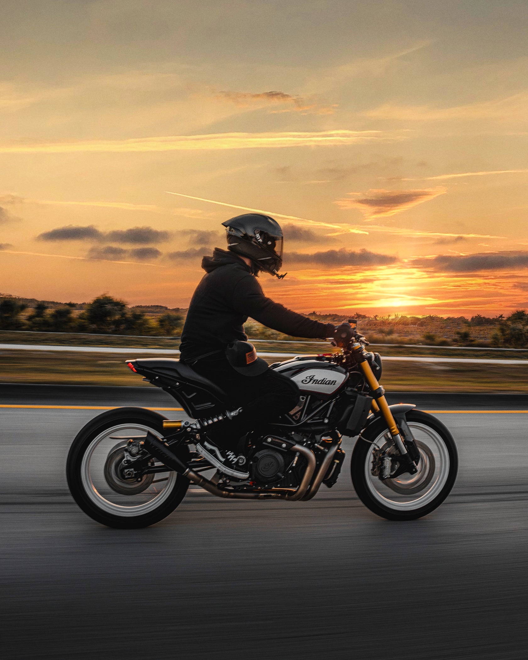 Motorcyclist riding an Indian motorcycle at sunset on an open road.