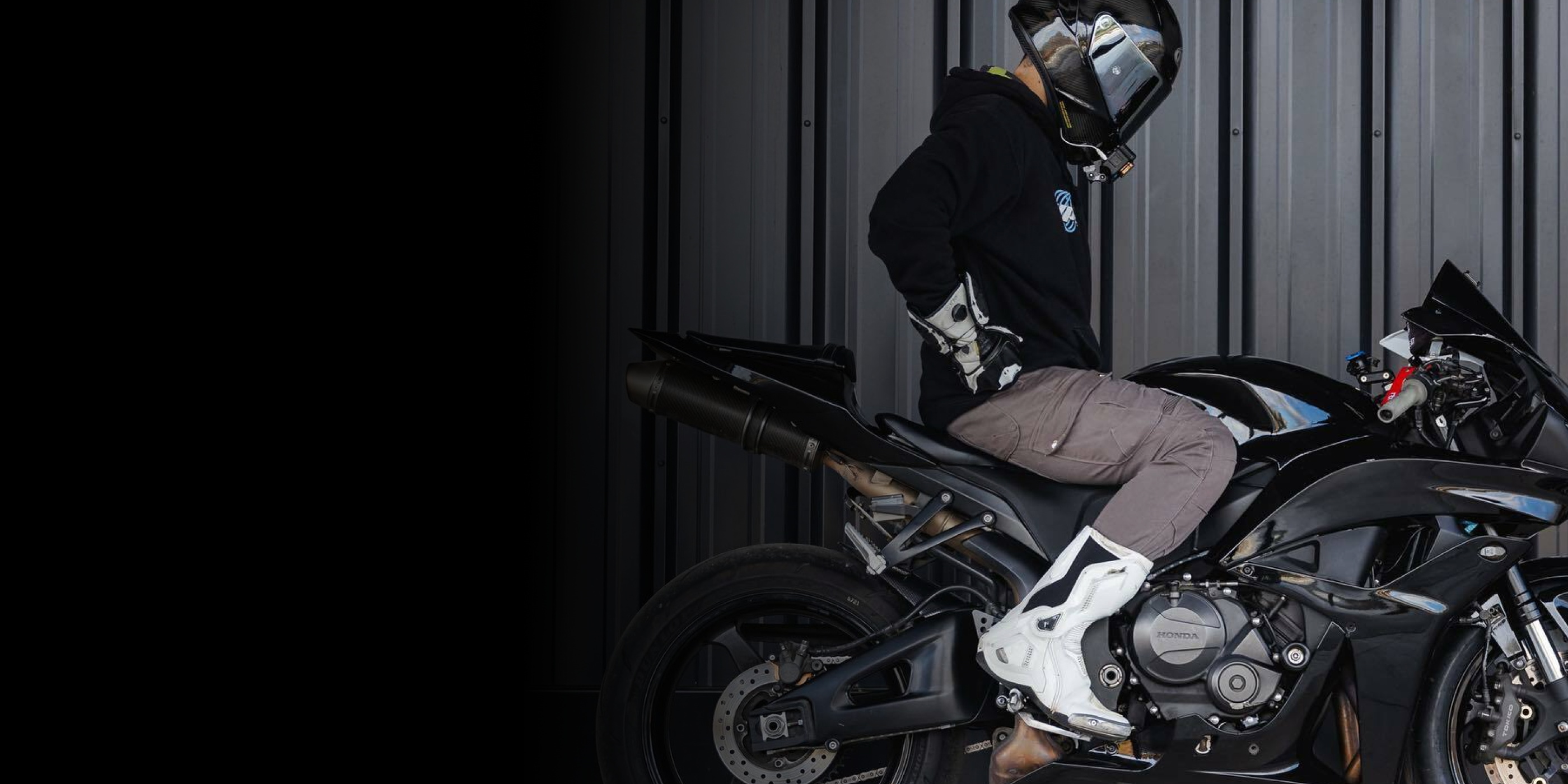 Motorcyclist in protective gear sitting on a black sports bike against a grey striped background.