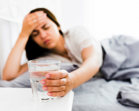 Mujer alcanzado un vaso de agua y con dolor de cabeza
