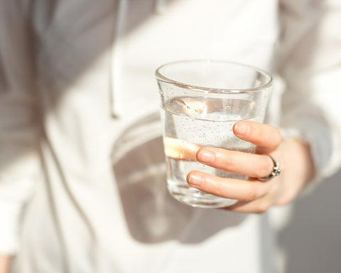 Mano sosteniendo vaso con agua en fondo blanco.