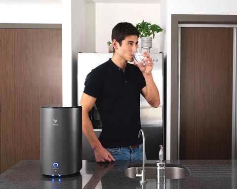 Hombre bebiendo agua pura de un vaso en una cocina con un purificador.