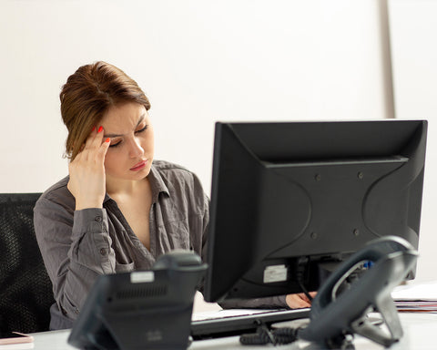 Mujer con blusa negra tocándose la cabeza enfrente de la computadora.