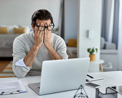 Hombre con las manos en sus ojos y enfrente su computadora